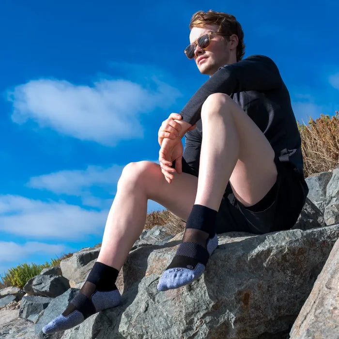 Man sitting on rock wearing black active comfort sock in quarter crew height | OS1st