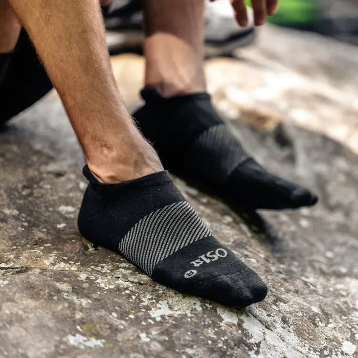 person wearing black wicked comfort merino wool performance sock no show length while sitting on rock outdoors | OS1st